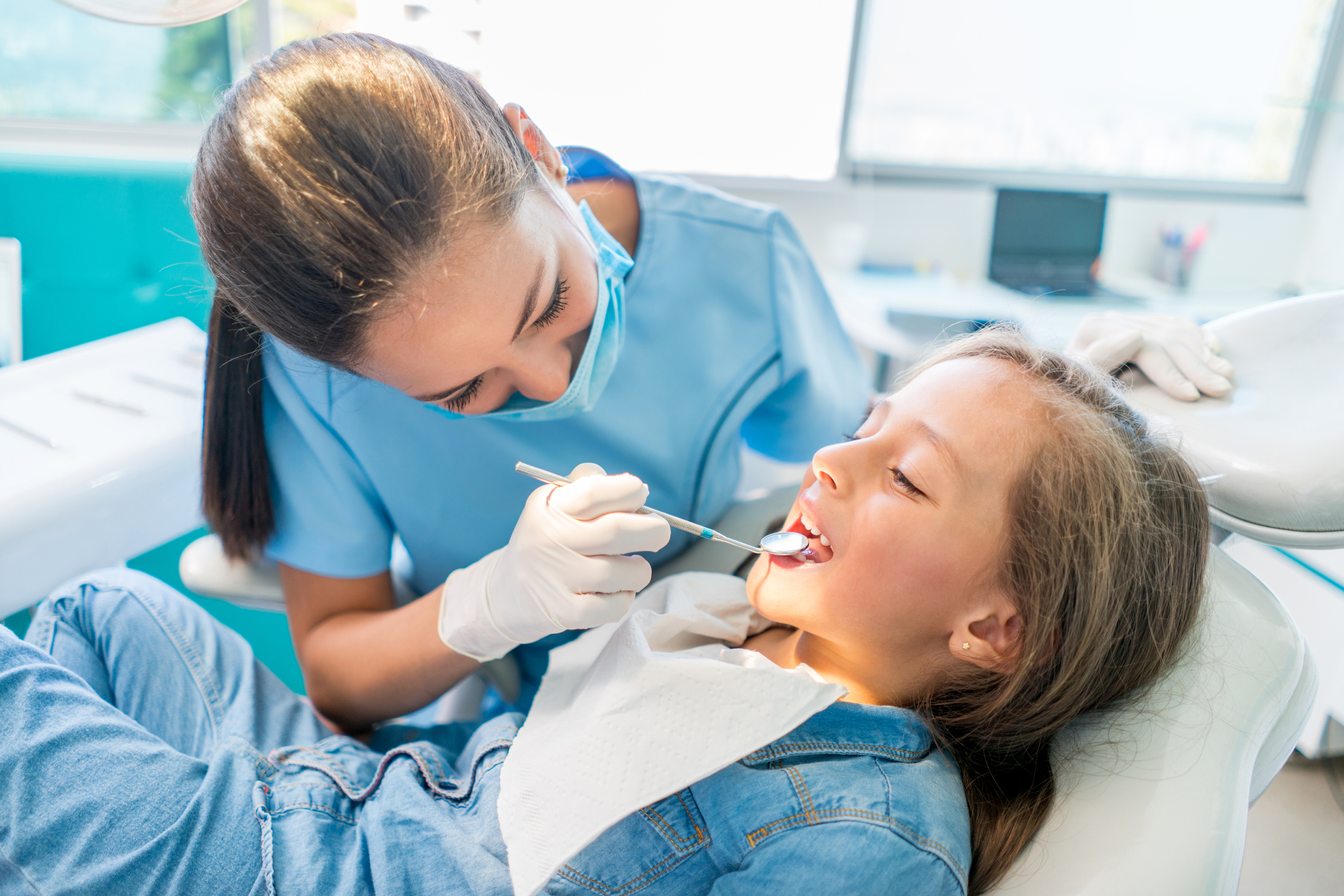 Female dentist wearing a mask and examining a pediatric female patient. Female dentist wearing a mask and examining a pediatric female patient.