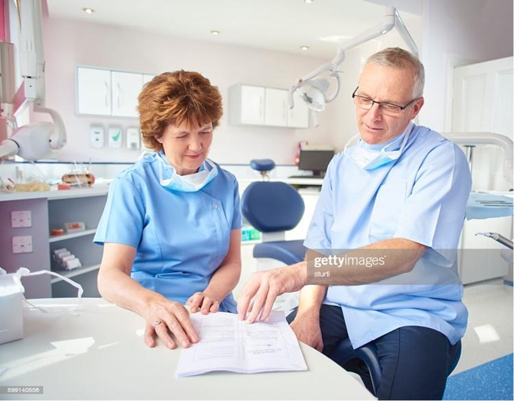 A male and female dentist sit in a dental office as they peruse paperwork and discuss dental practice membership programs. A male and female dentist sit in a dental office as they peruse paperwork and discuss dental practice membership programs.