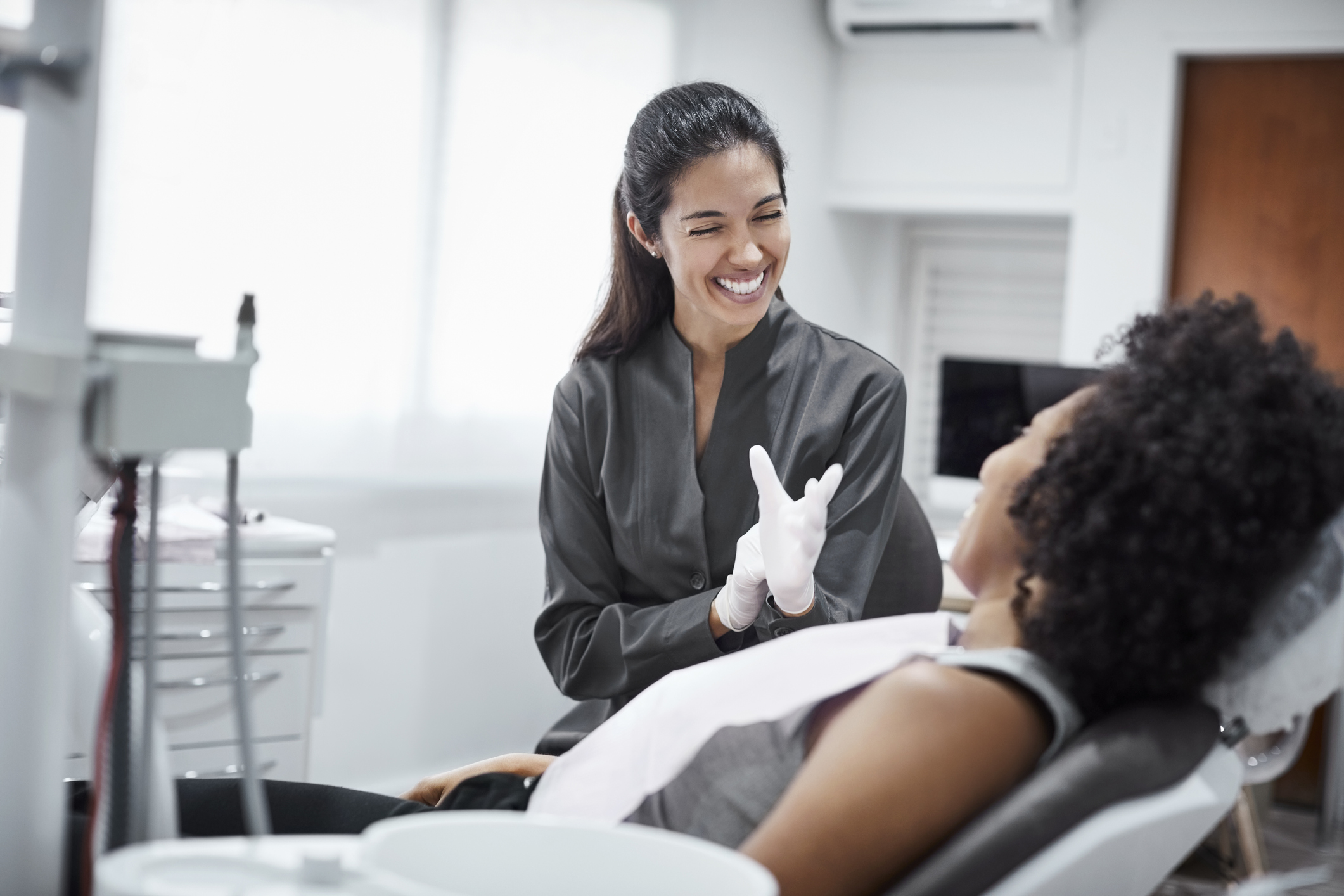 Female dentist putting on latex gloves and smiling at a patient in a dental chair