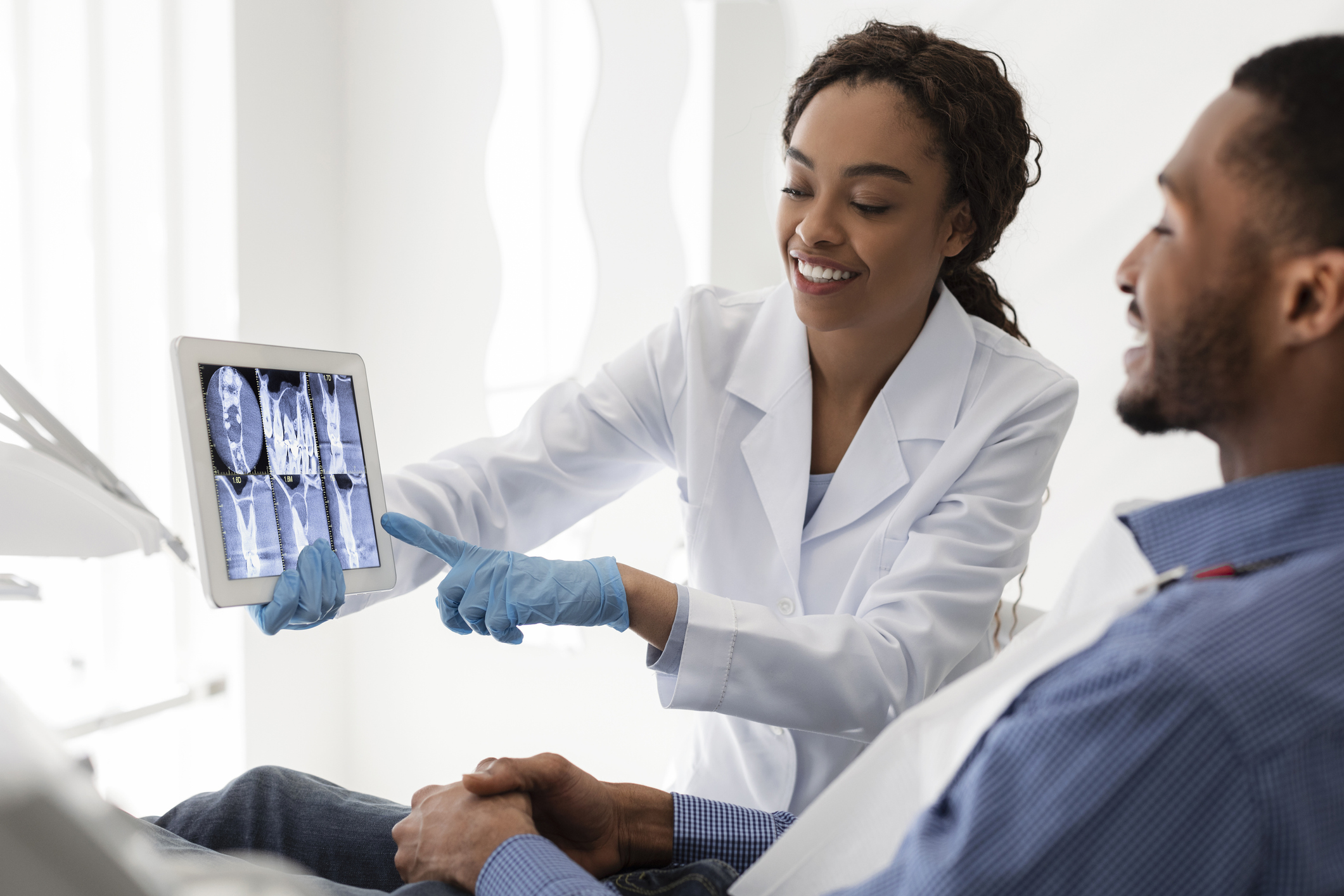 A female dentist shows dental scans on a tablet to a patient seated on a dentist’s chair as part of a broader customer or patient advocacy strategy.